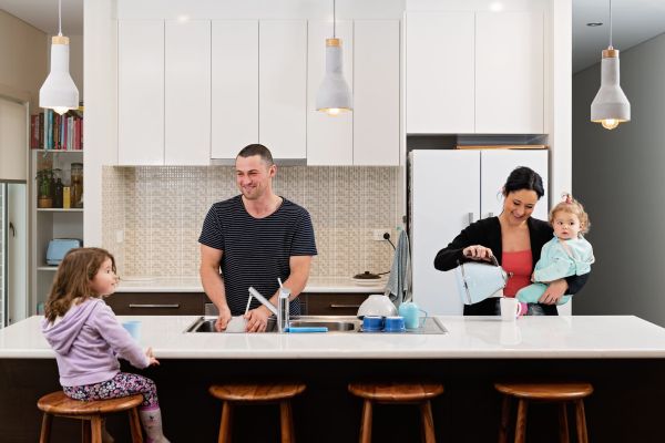 Family of four in the kitchen. Dad is washing dishes and Mum is pouring water from a kettle into a mug